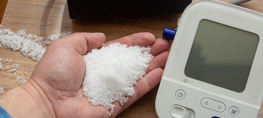 wooden spoon of salt beside blood pressure monitor showing the relationship between sodium intake and hypertension
